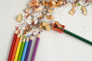 Colorful pencils with scattered shavings and a sharpener on white background, representing creativity, art, and back to school themes.