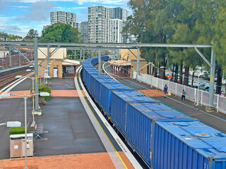 Long blue freight train going past a city train station