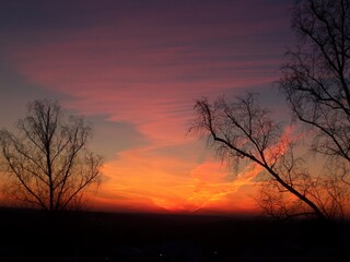 Naklejka premium Dramatic sunset sky, vibrant orange and purple hues, silhouetting bare trees or representing evening beauty