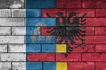 colourful painted big national flag of canary islands and flag of albania on a massive old brick wall background. concept