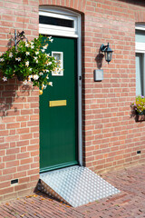 Brick house with green entrance door and wheelchair ramp at one entrance door. The entrance is suitable for disabled people.