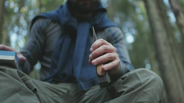 A man sharpens his axe deep in the forest. Sustainable survival concept focused on eco-friendly tools and living in harmony with nature.