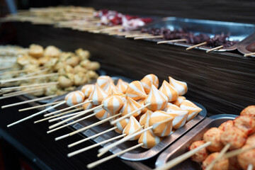 Close-up of skewered street food with focus on colorful fish balls, ready to be cooked, offering a variety of textures and flavors.