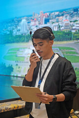 Asian male stage manager directs the show on stage using a headset, walkie-talkie, and clipboard,...