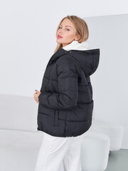 Young woman with long hair faces left, wearing a black padded jacket and white pants. Her head...