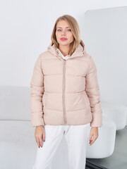 Blonde woman with shoulder-length hair wearing a beige puffer jacket, standing confidently in a...