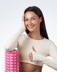 Smiling Sport Woman Holding Foam Roller And Giving Thumbs Up In Studio