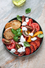 Salad with heirloom tomatoes, yogurt dressing and basil, vertical shot on a grey and roseate granite background, elevated view