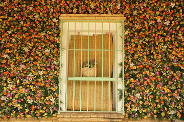 old window framed by many plastic flowers as decoration      