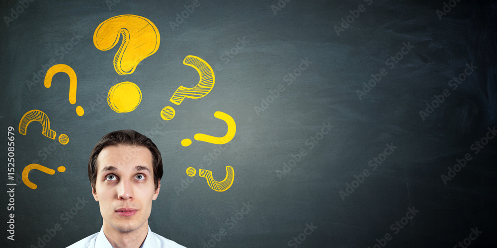Aufkleber Thoughtful man looking up at yellow question marks on blackboard background with copy space for education or problem-solving concept.