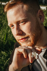 A young red-haired man with a beard in a blooming apple orchard, close-up.