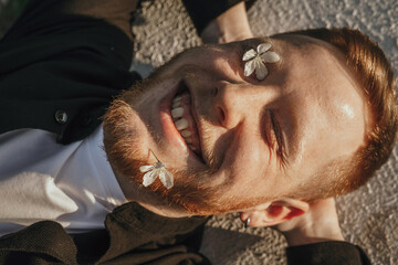 Portrait of a laughing man lying down with a flower in his beard on a summer day.