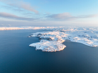 Aerial view of snow-covered islands emerging from the calm waters of the Barents Sea in the Arctic,...