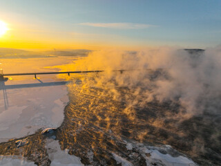 Aerial view of a frozen river with steam rising from its surface, illuminated by the golden light of a winter sunset, near Murmansk, Russia