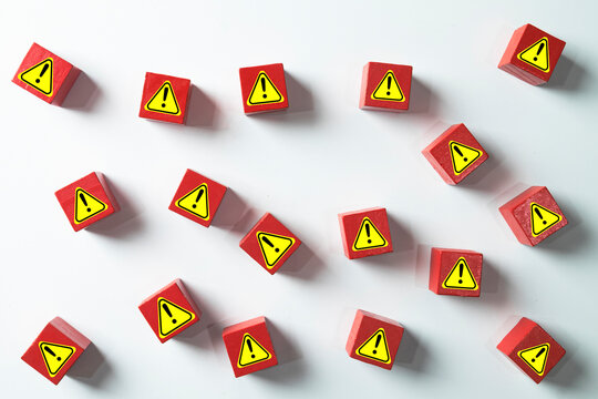 Red wooden blocks with yellow warning sign icons scattered on a white background. Concept for multiple risks, danger alerts, safety hazards, problem identification.