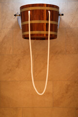 Traditional wooden bucket shower with pull rope, mounted on a tiled wall, commonly used in spas and...