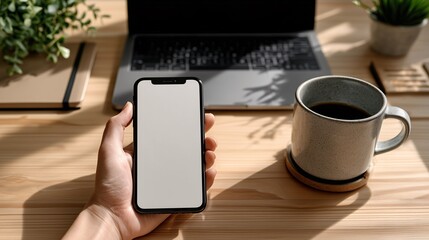 Smartphone in hand mockup with coffee cup and laptop on desk