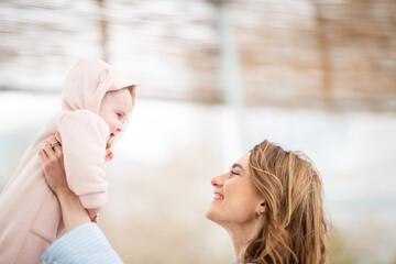 happy mother smiling as she lifts her baby dressed in a soft pink hooded outfit