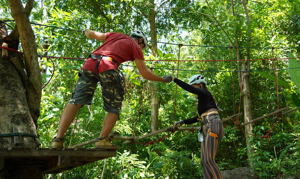 A man and a woman is walking across a challenging ropes course in the extreme park