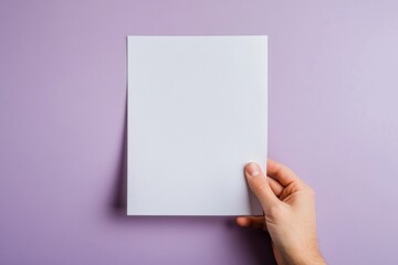 A hand holding a blank white sheet of paper against a pastel purple background. Useful for mockups, message display, or minimal graphic design concepts.