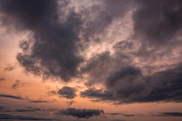 Cloudy sunset background backdrop with the orange sun breaking through the clouds.