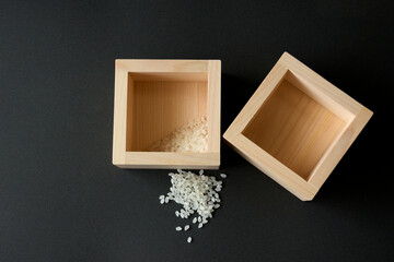 黒背景に少しのコメが入った升とこぼれたコメ