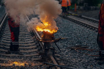 A worker in the process of a railroad track weld repair, reconstruction with a freight train passing