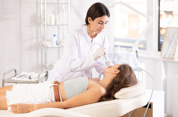 Fototapeta premium Brunette female doctor making facial beauty procedure with ice hummer to female patient