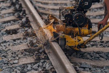 A worker in the process of a railroad track weld repair, reconstruction with a freight train passing