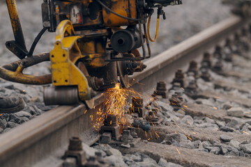 A worker in the process of a railroad track weld repair, reconstruction with a freight train passing