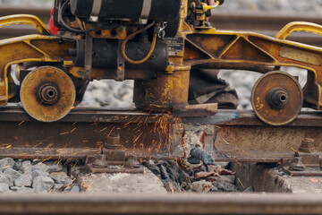 A worker in the process of a railroad track weld repair, reconstruction with a freight train passing