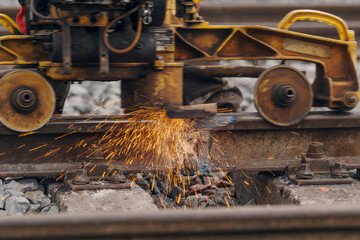 A worker in the process of a railroad track weld repair, reconstruction with a freight train passing