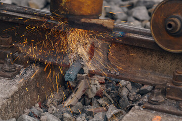 A worker in the process of a railroad track weld repair, reconstruction with a freight train passing