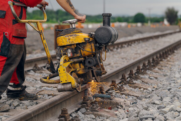 A worker in the process of a railroad track weld repair, reconstruction with a freight train passing