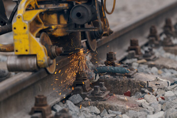 A worker in the process of a railroad track weld repair, reconstruction with a freight train passing