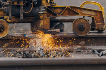A worker in the process of a railroad track weld repair, reconstruction with a freight train passing