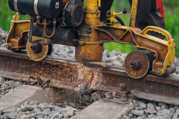 A worker in the process of a railroad track weld repair, reconstruction with a freight train passing