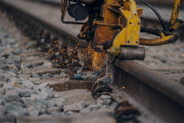 A worker in the process of a railroad track weld repair, reconstruction with a freight train passing