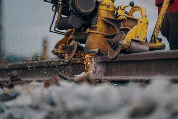 A worker in the process of a railroad track weld repair, reconstruction with a freight train passing