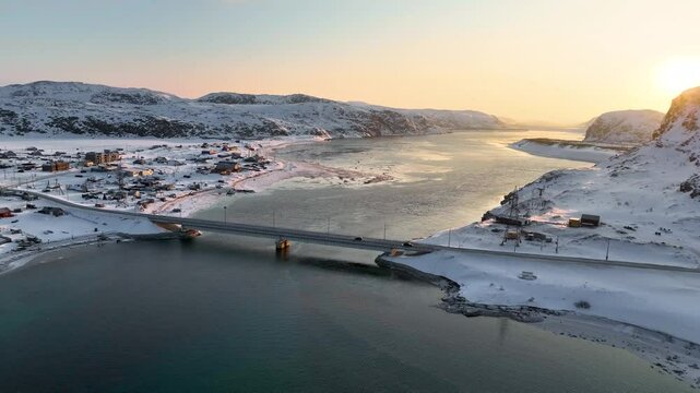 Panoramic aerial view of a snowy coastal village nestled among hills leading to the open sea in Teriberka, Russia