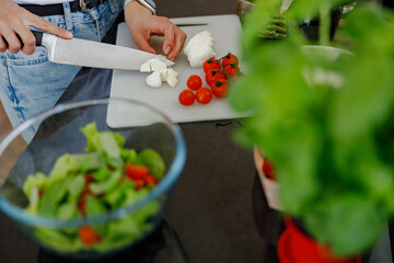 In a cozy kitchen, a skilled person prepares fresh tomatoes, mozzarella cheese, and a colorful salad