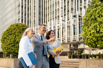Three colleagues reviewing documents outside a modern office complex