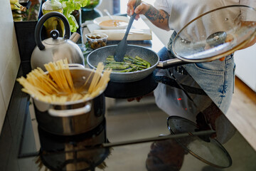In a modern kitchen, a person skillfully cooks pasta and fresh vegetables, showcasing their culinary expertise