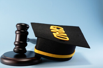 close up of wooden gavel hammer and mortar board against blue background