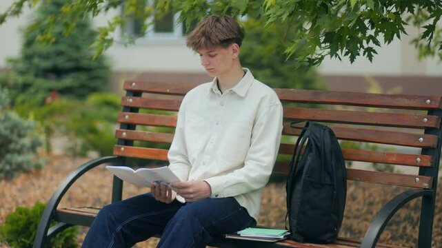 Teen student studying quietly on a park bench with backpack beside