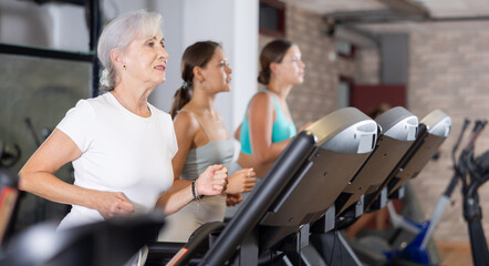 Elderly woman in sportswear are running on treadmill in crossfit gym. Physical activity, healthy lifestyle. Easy and simple weight loss, affordable workouts, active self-care