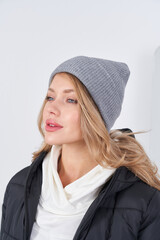 A woman with long hair and blue eyes is wearing a gray knit beanie, a white scarf, and a black...
