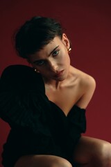 Naklejka premium Model poses gracefully in black outfit against rich red backdrop in an artistic studio setting