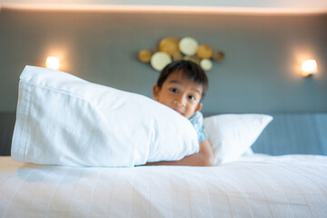 Little kindergarten boy enjoying play on white bed pillow hotel room