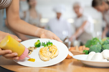 Close-up of woman pouring sauce into prepared chicken dish at master class